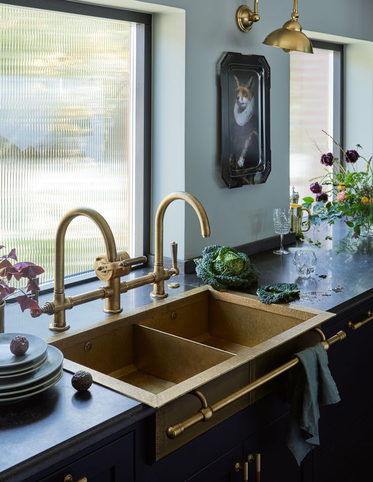 a kitchen sink with two faucets in front of it and flowers on the counter