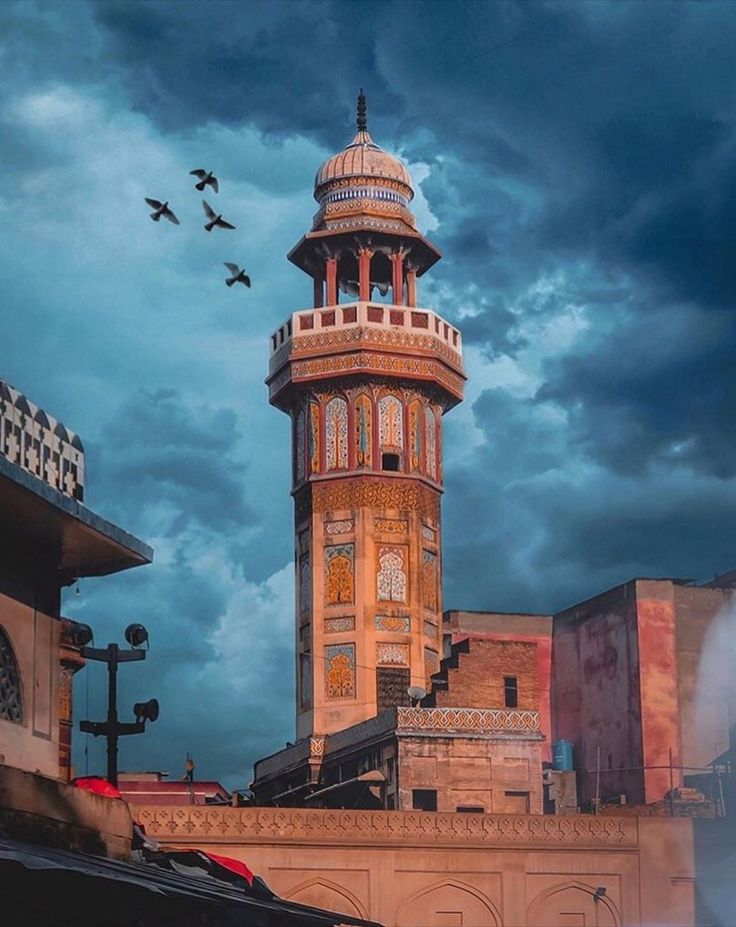 a tall tower with a clock on it's side and birds flying around in the sky