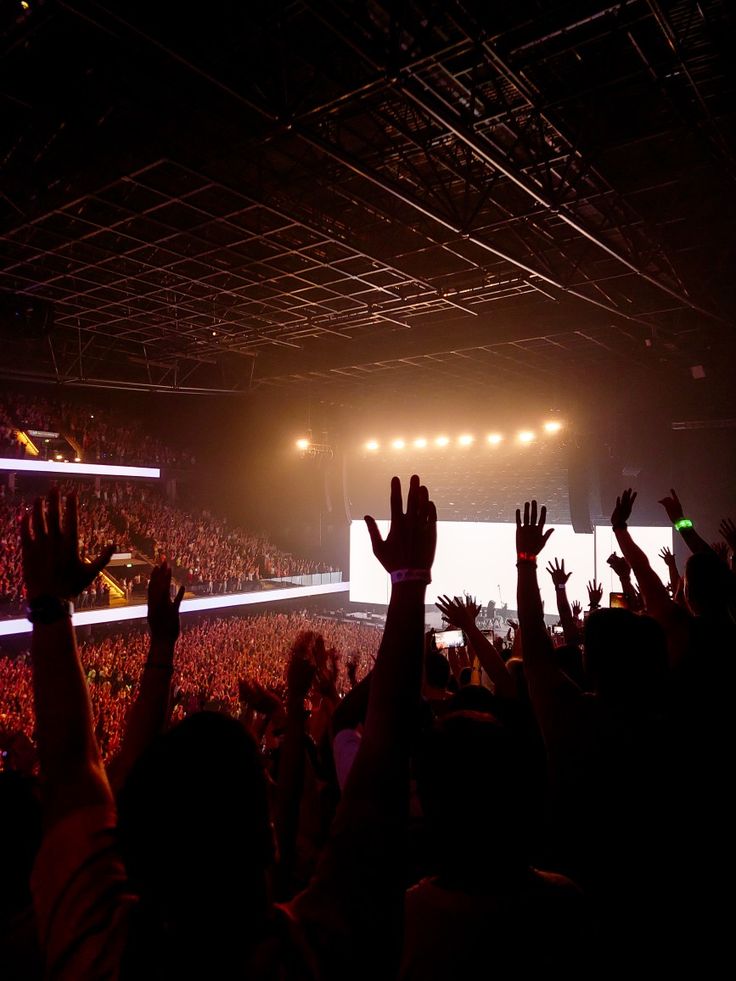 a crowd of people at a concert with their hands in the air and lights on