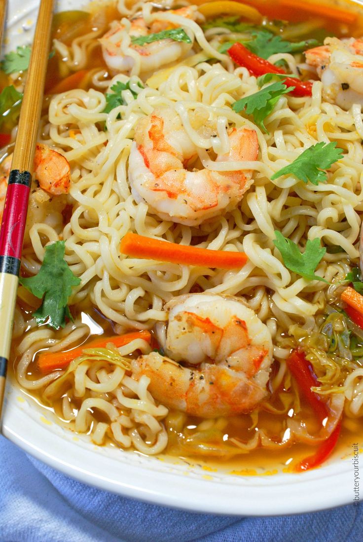 a white plate topped with noodles and shrimp next to chopsticks on a blue table cloth