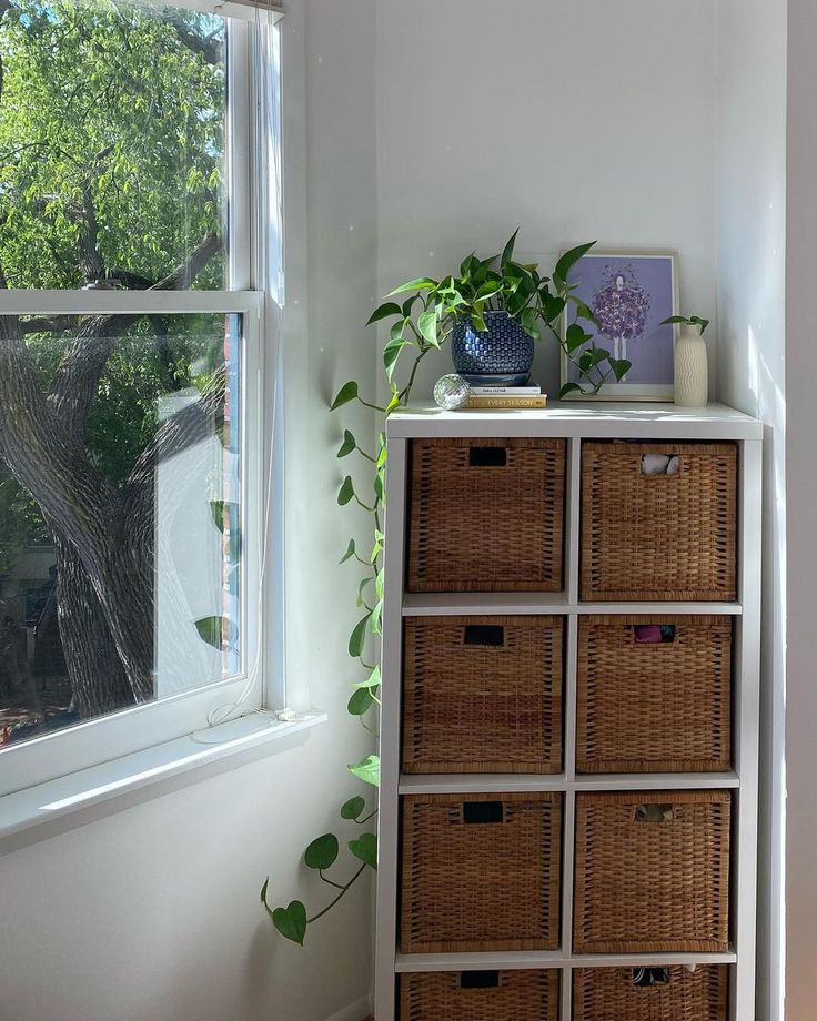 a room with a window, wicker drawers and plants on the shelf next to it