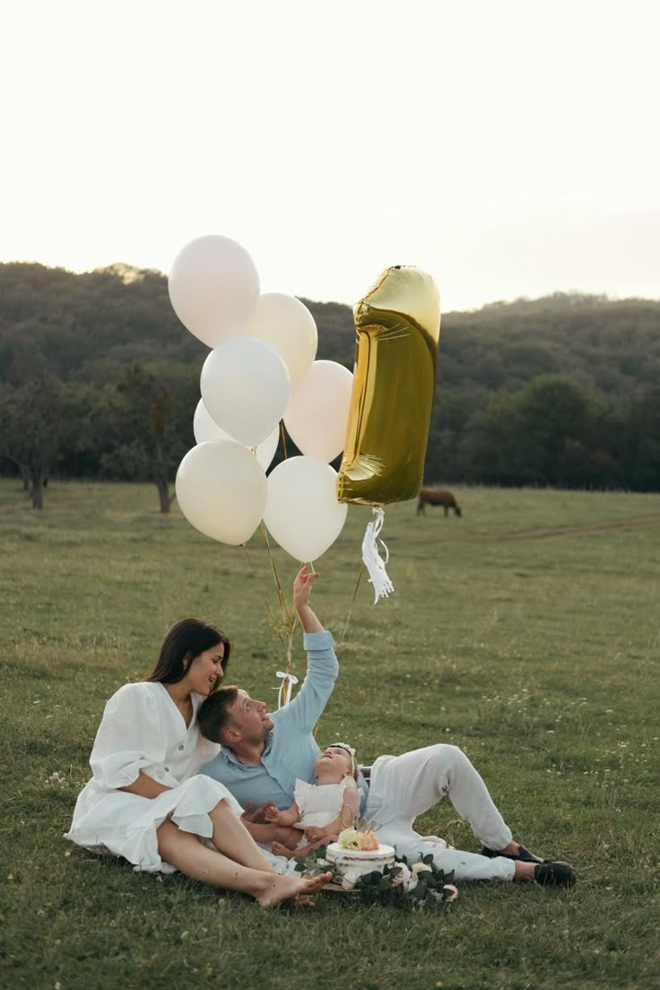 a man and woman sitting on the grass with balloons