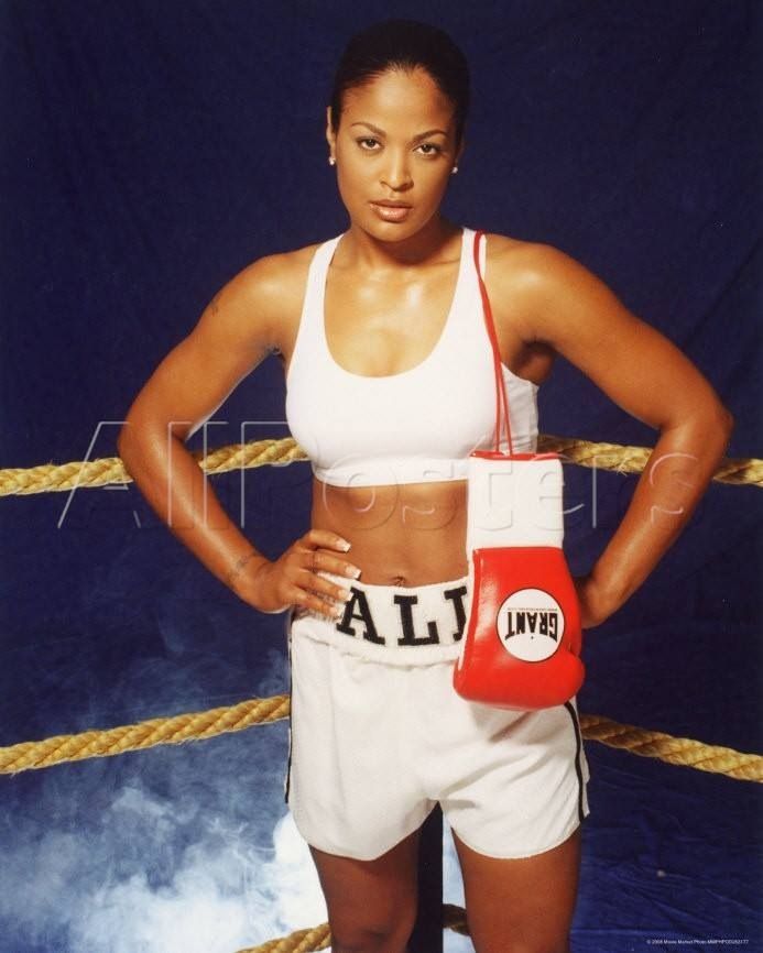 a woman standing in front of a boxing ring with her hands on her hips and holding a punching mitt