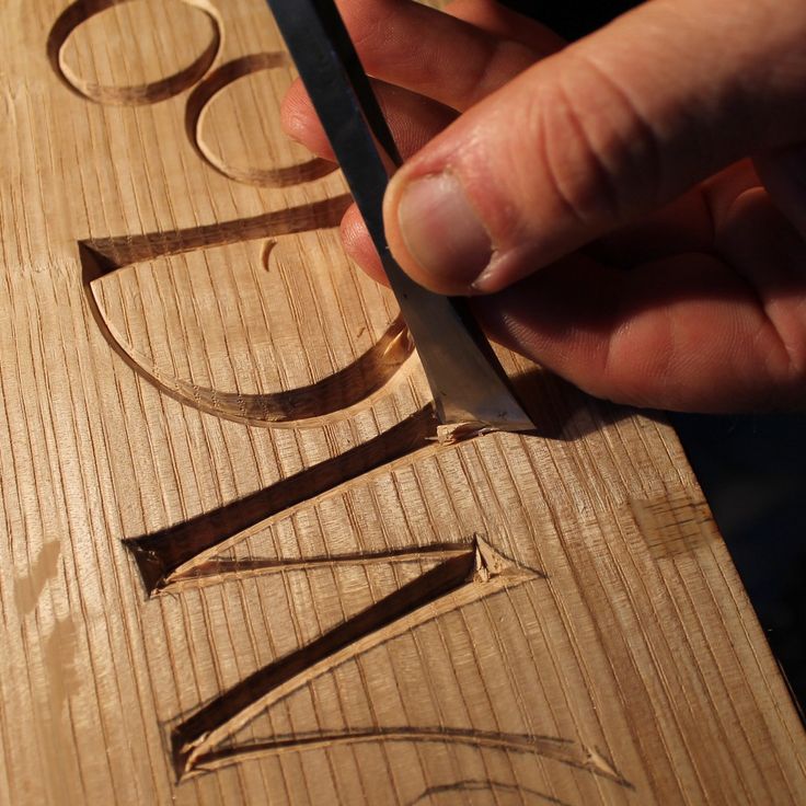 a person is carving the letters on a wooden board