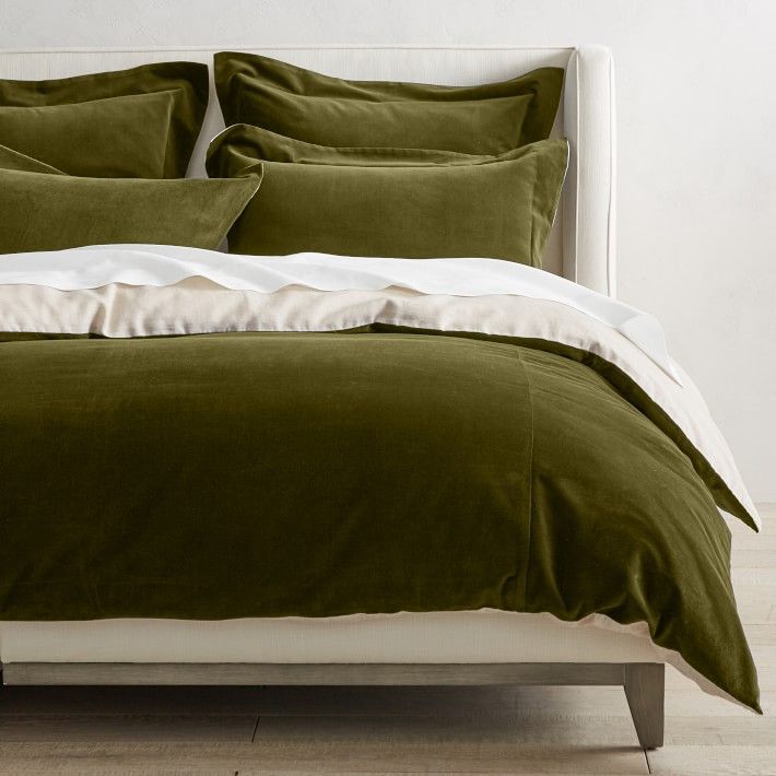 a bed with green and white linens in a minimalistic bedroom setting, including the headboard and foot board