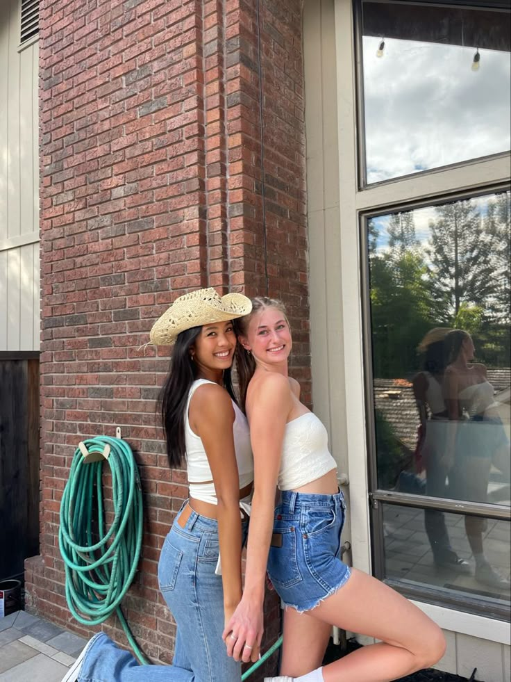 two women standing next to each other in front of a brick building wearing cowboy hats