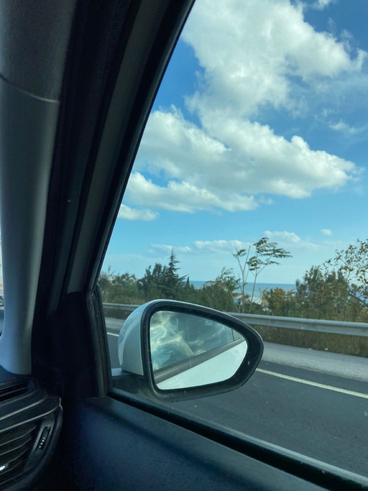 the view from inside a car looking out at an ocean and clouds in the sky