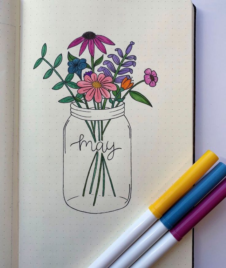 an open notebook with flowers in a mason jar on it and three markers next to it