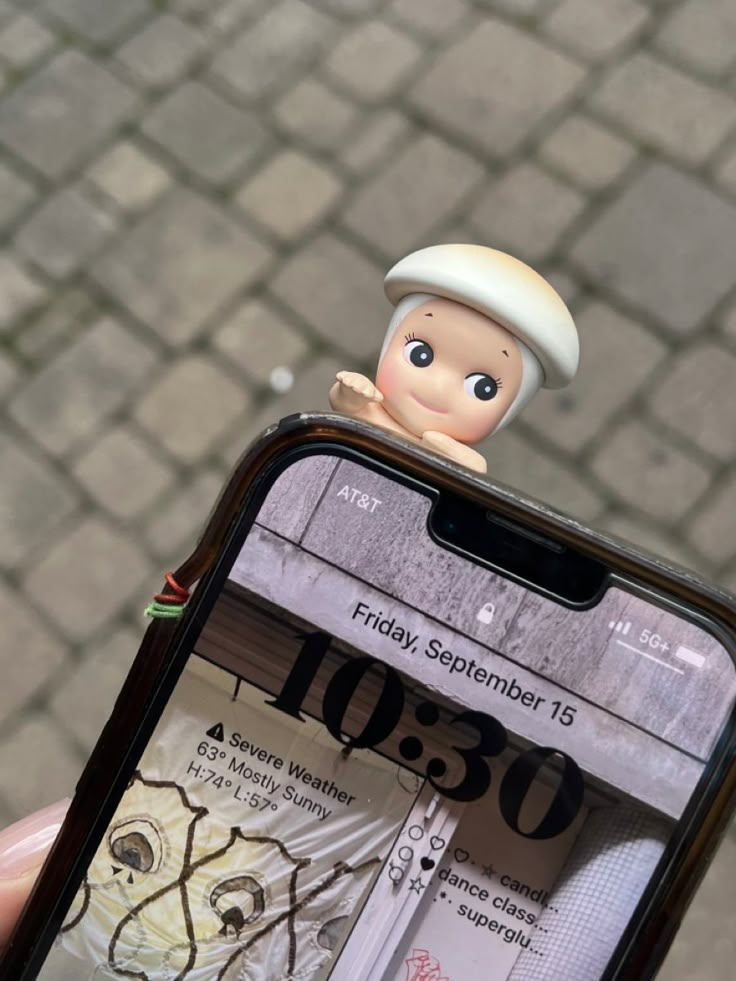 a person holding up a cell phone with a small doll on top of the screen