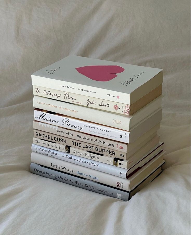 a stack of books sitting on top of a white bed covered in sheets and pillows