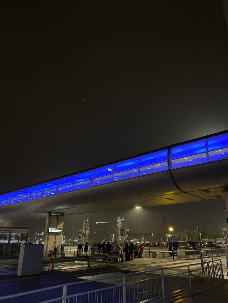 people are standing outside at night under an overpass with blue lights on the side