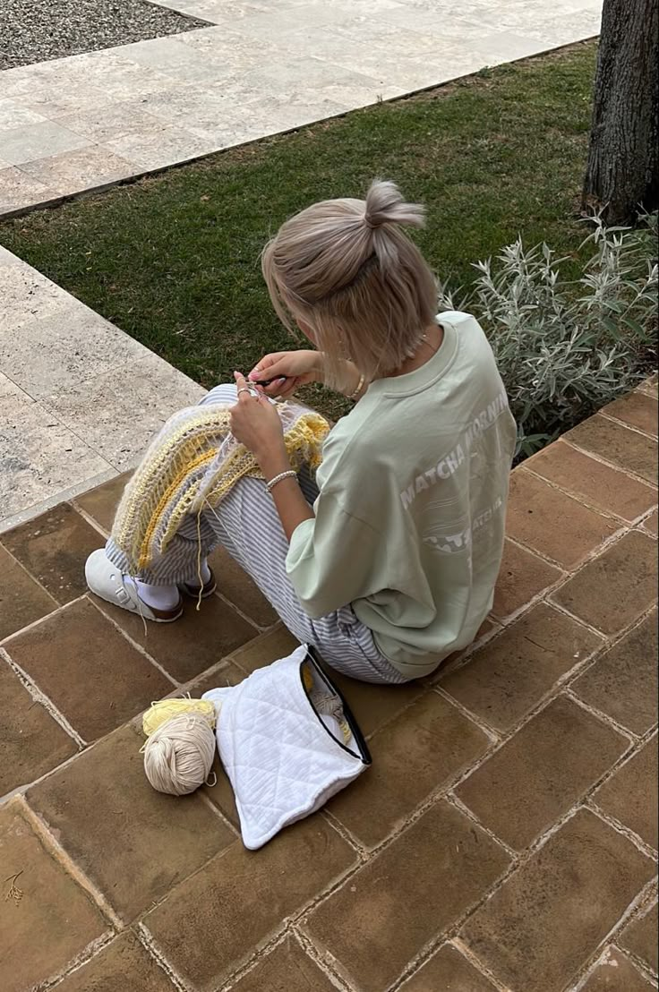 a woman sitting on the ground knitting