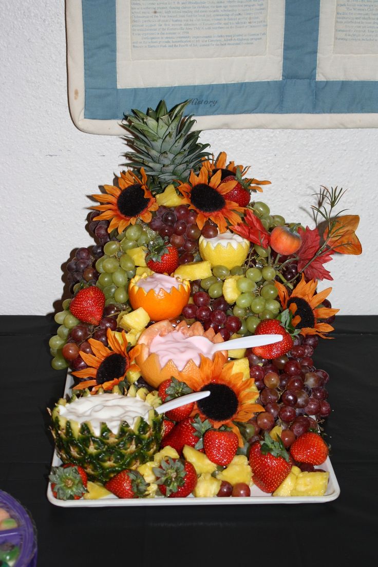 a fruit pyramid is displayed on a table with grapes, strawberries, pineapples and oranges