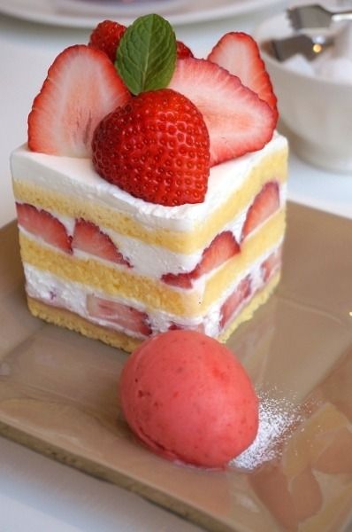 a piece of cake with strawberries on top is sitting on a plate next to an ice cream ball