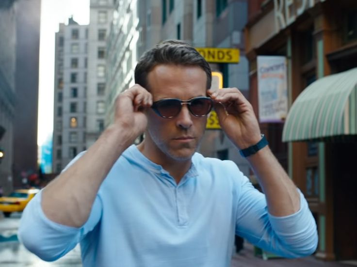 a man in sunglasses is standing on the street with his hands to his ears and looking at something