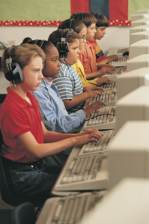 several children sitting at computers with headphones on and one child using the computer keyboard