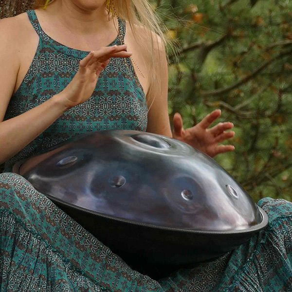 a woman sitting on the ground with a large object in her hand and trees behind her