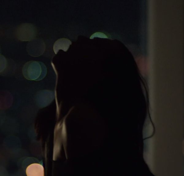 a woman standing in front of a window at night with her head tilted to the side