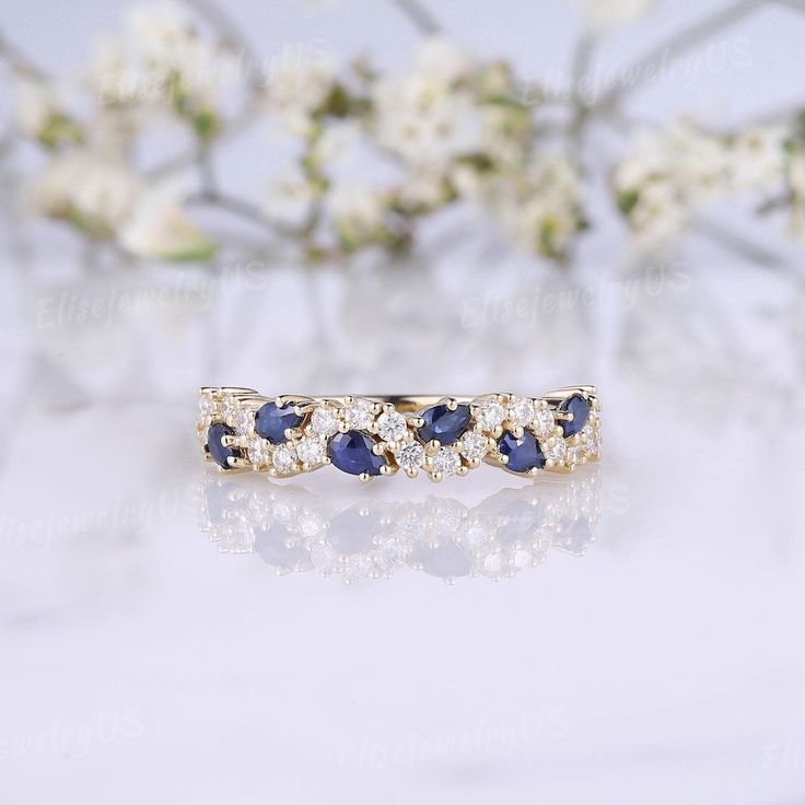 a diamond and blue sapphire band ring sitting on top of a white table next to flowers