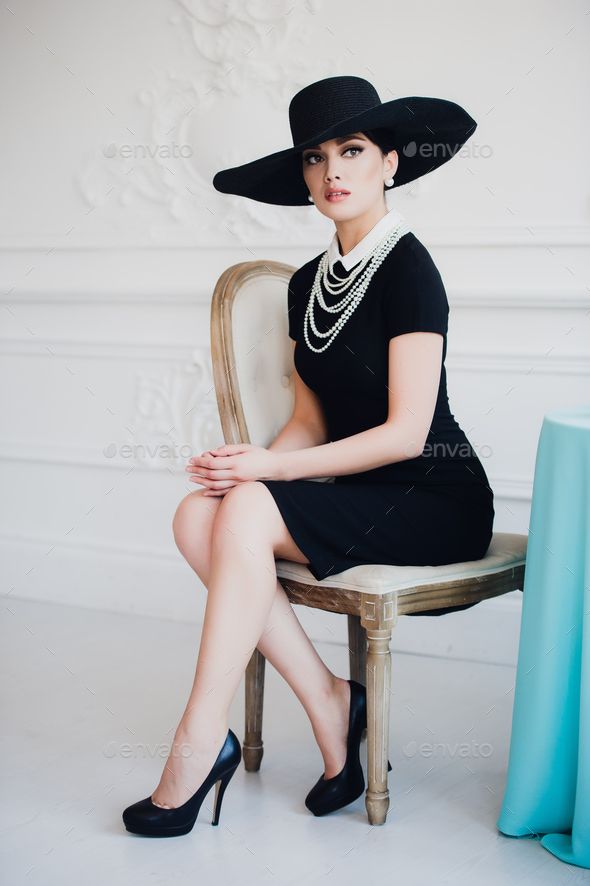 a woman in a black dress and hat sitting on a chair - stock photo - images