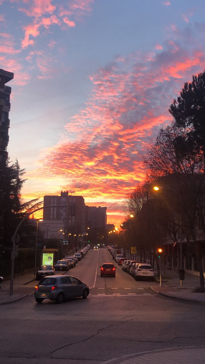 cars are parked on the street as the sun sets in the sky over some buildings