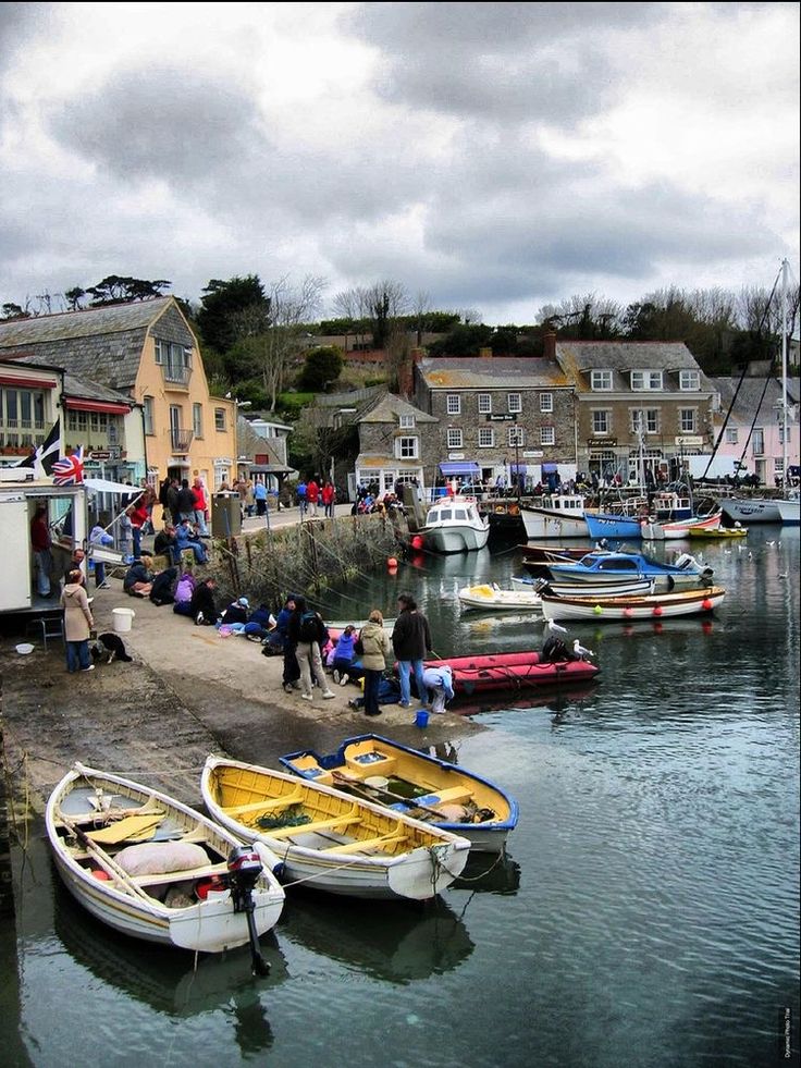 several small boats are docked in the water near some buildings and people walking around them