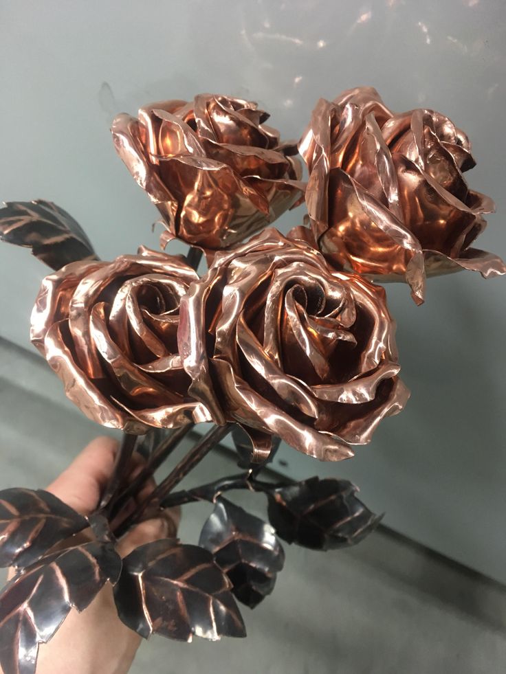 a person holding some metal flowers in their hand and it looks like they have been made out of copper foil