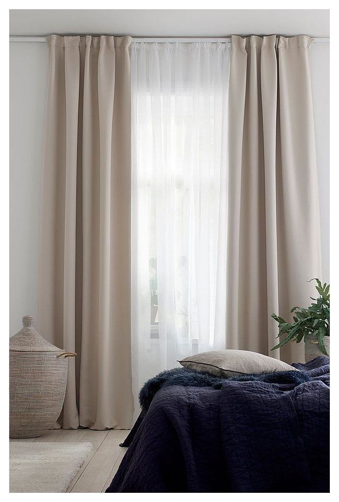 a bed sitting next to a window with curtains on it's sides and a potted plant in the corner