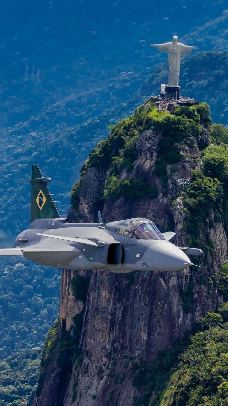 a fighter jet flying in front of a statue on top of a mountain