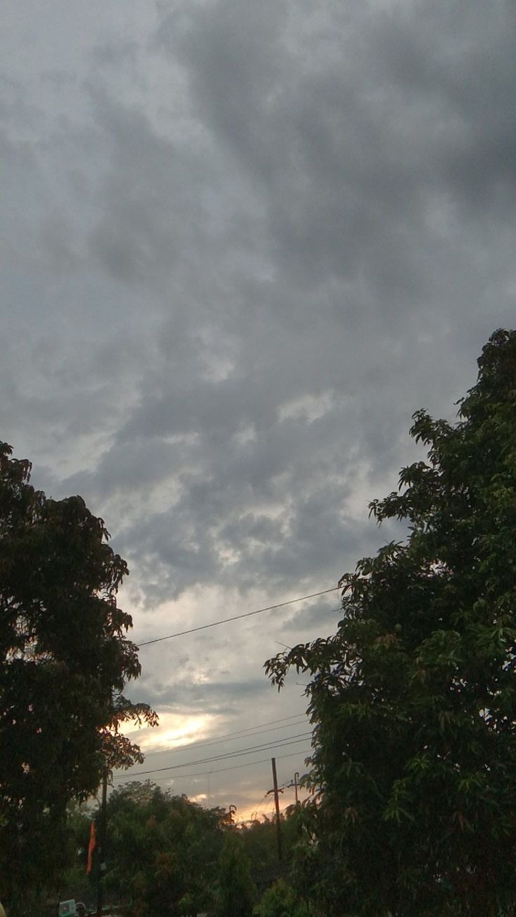 the sky is very cloudy and there are trees on the side of the road in front of it