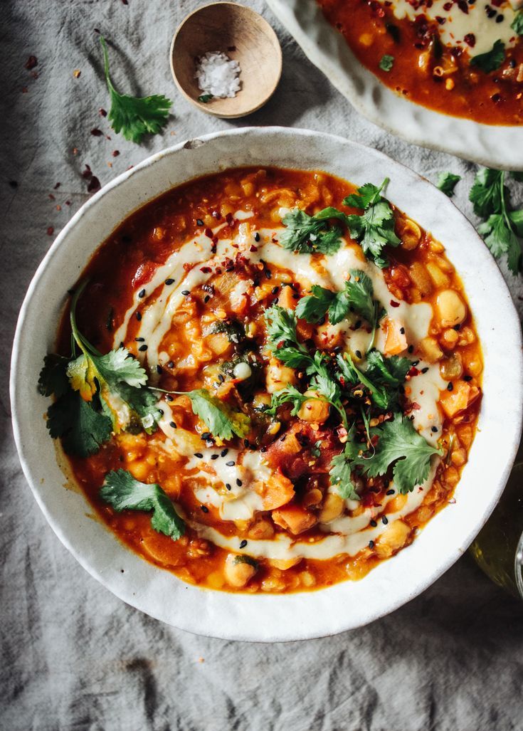 two white bowls filled with soup and garnished with cilantro, parsley