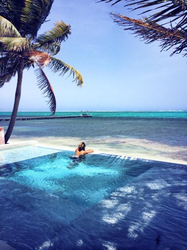 a woman in a swimming pool surrounded by palm trees and the ocean with a boat on the horizon