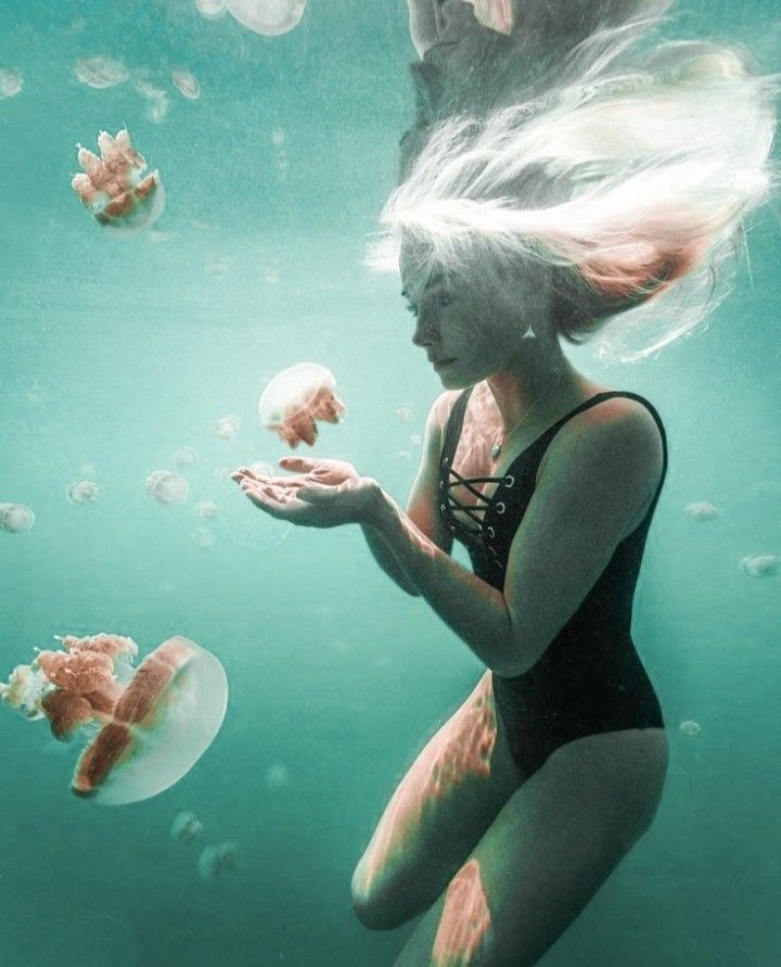 a woman in a black swimsuit under water with jellyfish