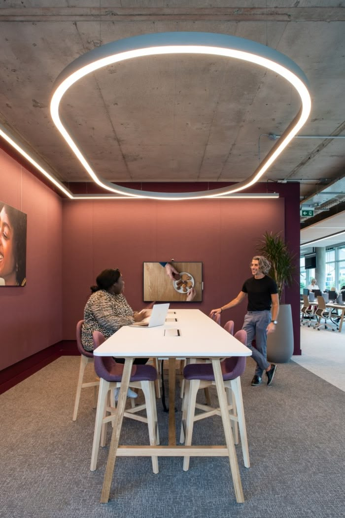 two people are sitting at a table in an office with pink walls and purple chairs