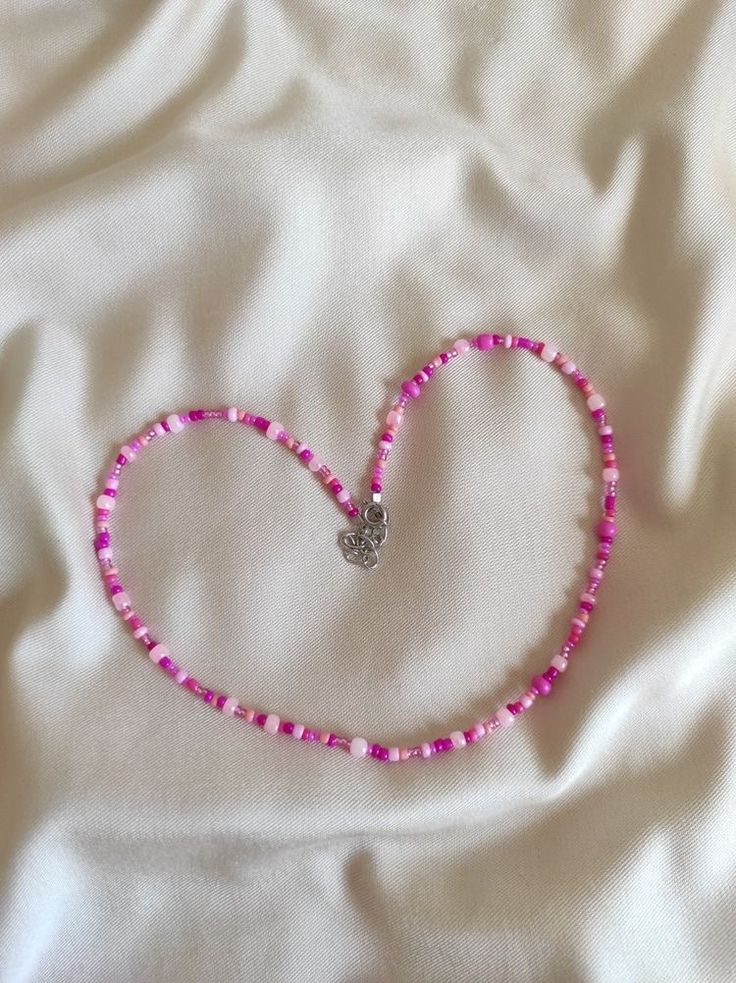 a pink beaded heart necklace laying on a white sheet with a small diamond in the middle