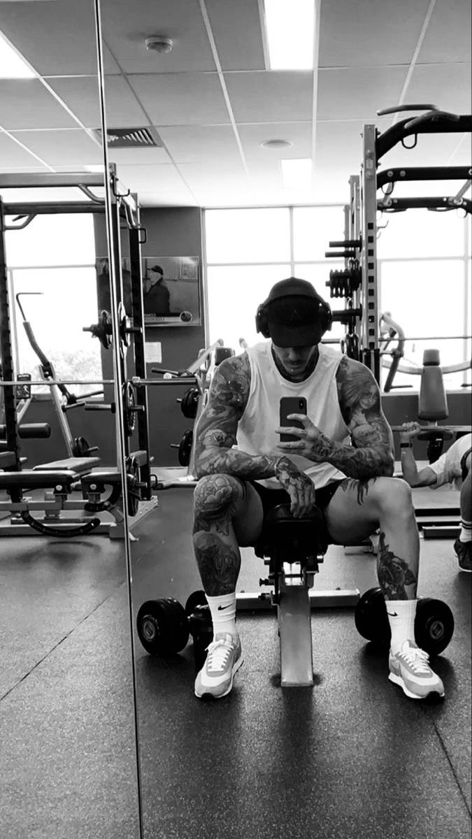 a man sitting on top of a bench in a gym holding a cell phone and looking at it