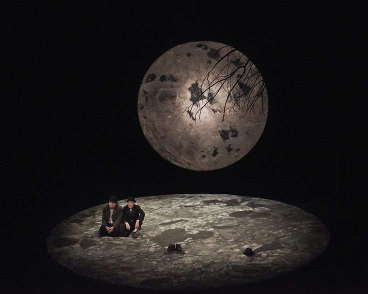 two people sitting on the ground in front of a full moon