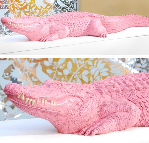 a pink alligator statue sitting on top of a white table next to a mirror with gold and silver wallpaper behind it