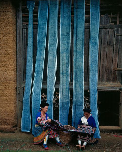 two women sitting on the ground in front of a building with blue curtained windows