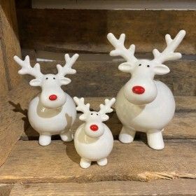 three white ceramic reindeer figurines with red nose and antlers sitting on wooden steps