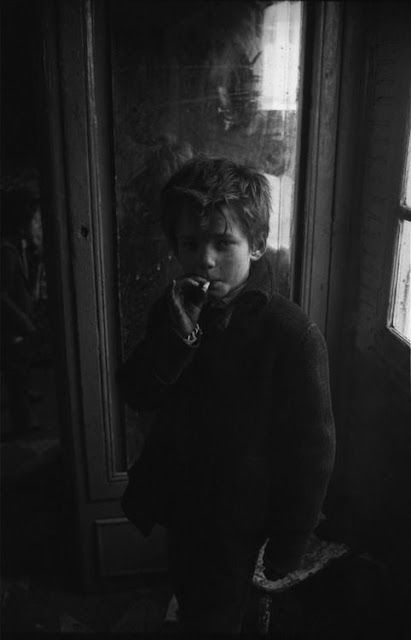 a young boy standing in front of a window with his hand on his mouth and looking at the camera