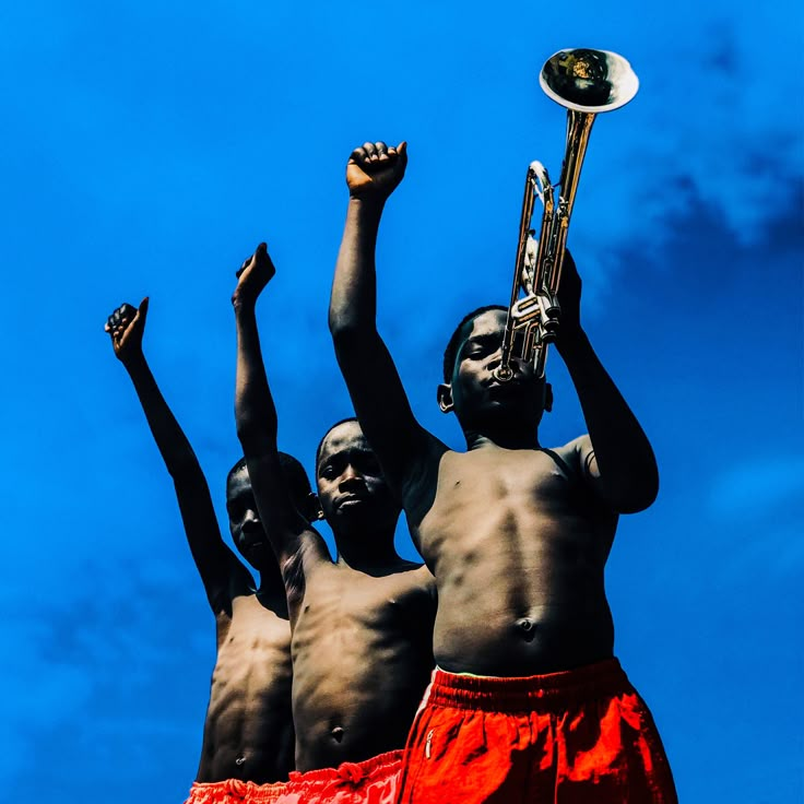 three men with their arms in the air, one holding a trumpet and another standing behind them