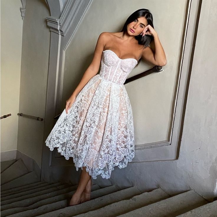 a woman in a white dress leaning against a wall with her hand on her head