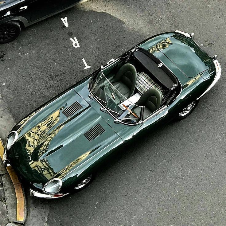 an old green sports car is parked on the street