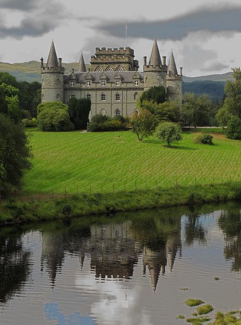 a large castle sitting on top of a lush green field next to a lake in front of it