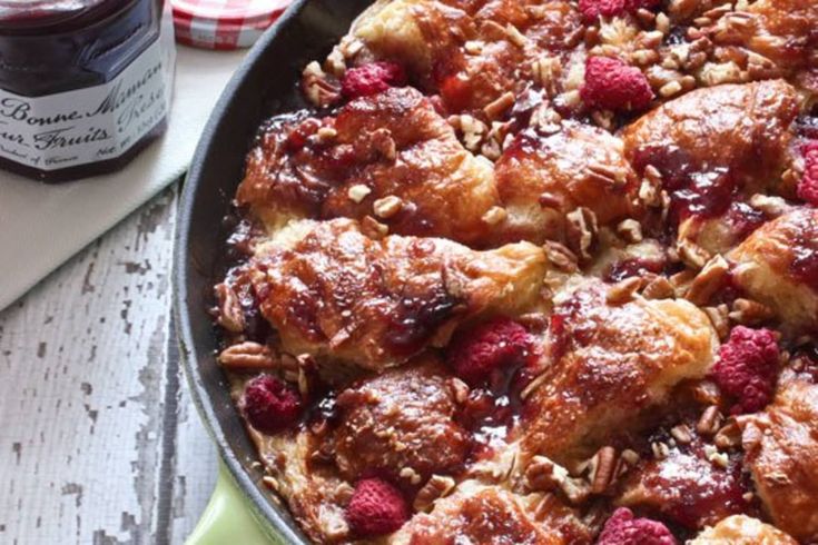 a pan filled with raspberry bread pudding next to a jar of jam on a table