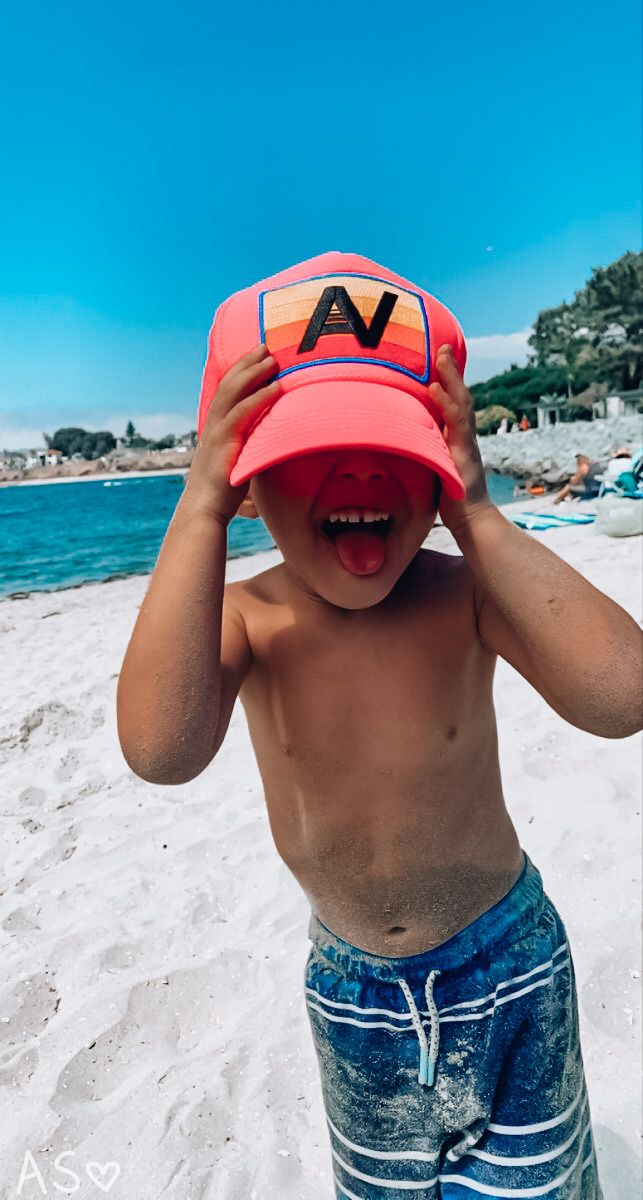 a young boy on the beach wearing a hat that says v is for v in front of his face