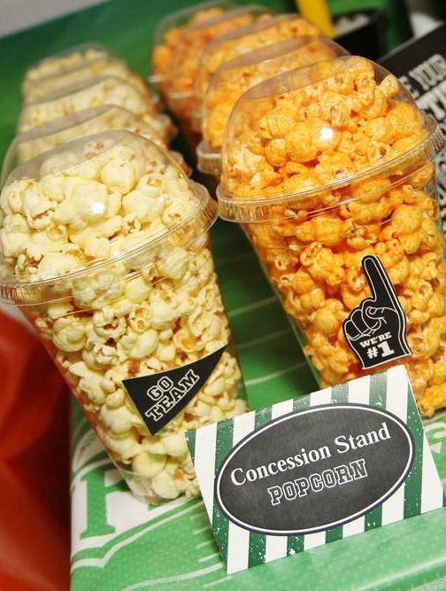 three plastic cups filled with popcorn sitting on top of a table next to a football field