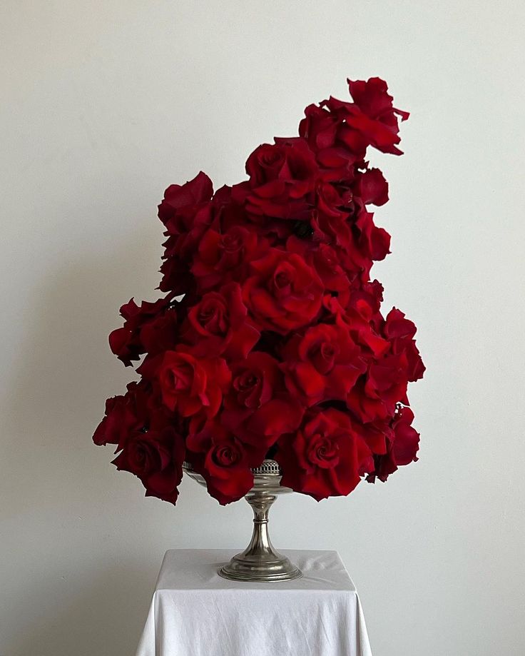 a silver vase filled with red roses on top of a white tablecloth covered table