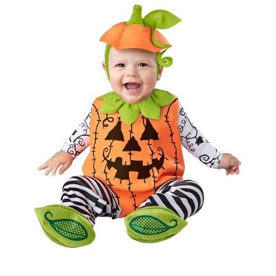 a baby in a pumpkin costume sitting on the ground with its mouth open and tongue out